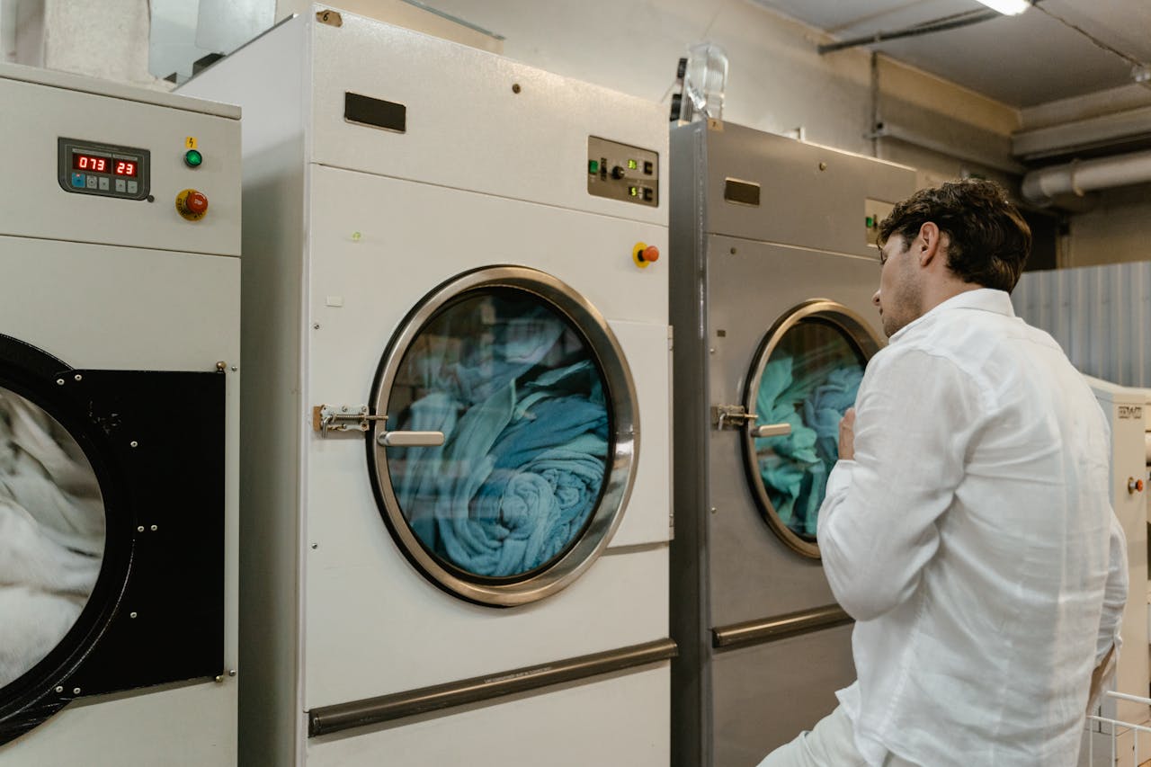 A man wearing a white shirt uses industrial washing machines in a public launderette.